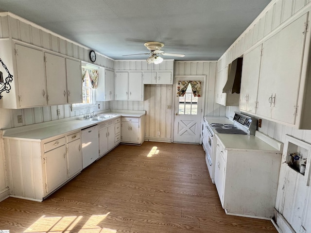 kitchen featuring a wealth of natural light, white appliances, wall chimney range hood, and wood finished floors