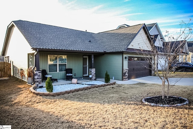 view of front of house with an attached garage, fence, stone siding, driveway, and roof with shingles