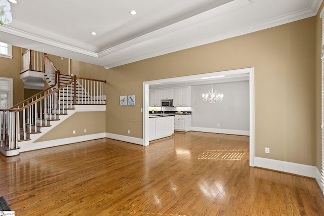 unfurnished living room featuring stairs, baseboards, a raised ceiling, and wood finished floors