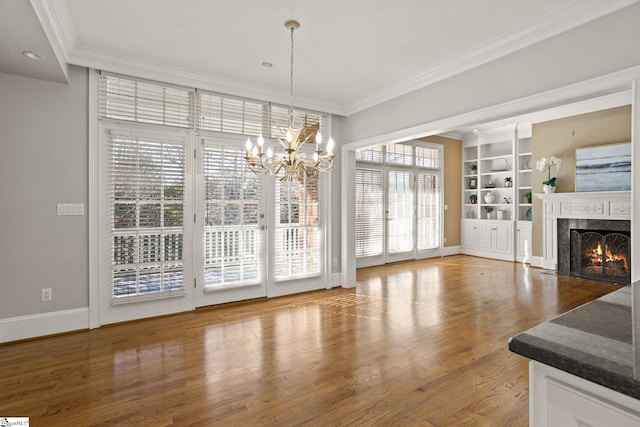 unfurnished dining area with built in shelves, a premium fireplace, ornamental molding, wood finished floors, and baseboards