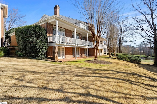 rear view of property with a yard, a chimney, a porch, and brick siding