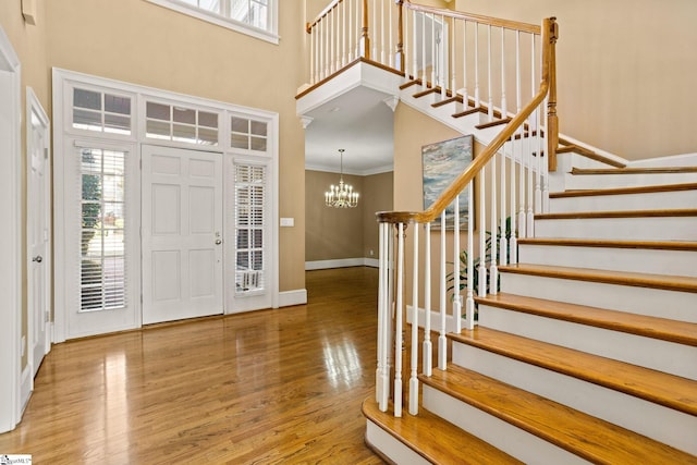 foyer featuring wood finished floors, baseboards, stairs, ornamental molding, and an inviting chandelier