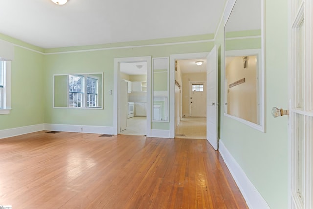 empty room with light wood finished floors, visible vents, and baseboards