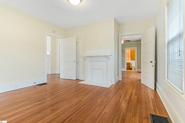 unfurnished living room with light wood-style floors, visible vents, ornamental molding, and baseboards