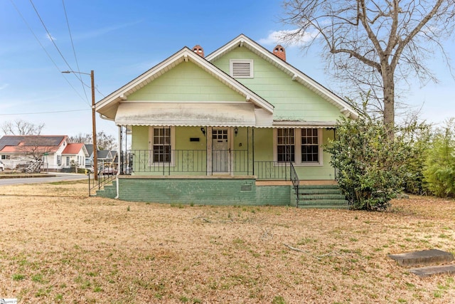 bungalow-style home with covered porch, a front lawn, and a chimney