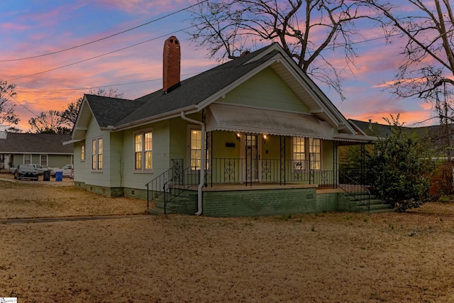 view of front of house featuring covered porch, roof with shingles, and a chimney