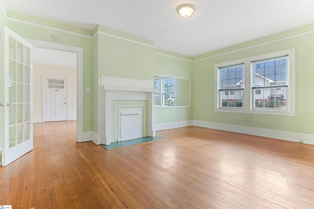 unfurnished living room featuring ornamental molding, a fireplace with flush hearth, hardwood / wood-style flooring, and baseboards