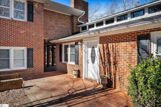 view of exterior entry featuring brick siding and a chimney