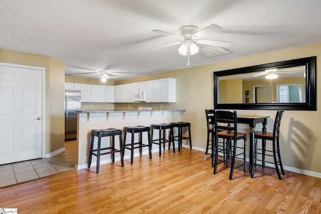 kitchen featuring a breakfast bar area, visible vents, white microwave, white cabinets, and stainless steel refrigerator