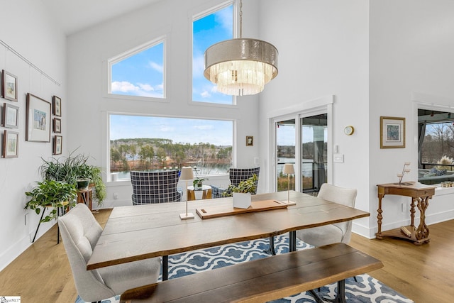 dining area featuring baseboards, a high ceiling, an inviting chandelier, and light wood-style floors