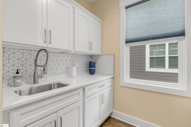 kitchen featuring tasteful backsplash, light countertops, white cabinetry, a sink, and baseboards