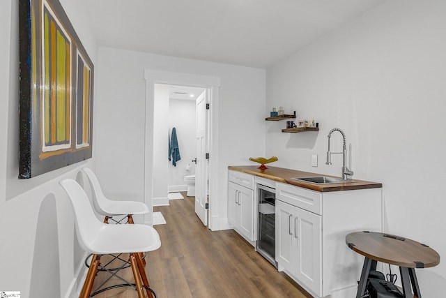 bar featuring wine cooler, a sink, baseboards, wet bar, and dark wood-style floors