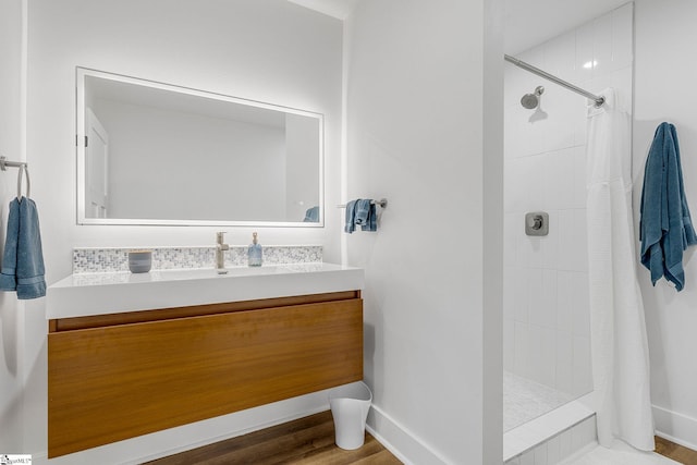 bathroom with wood finished floors, a tile shower, vanity, and baseboards