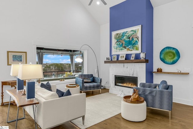 living room featuring a high end fireplace, ceiling fan, wood finished floors, high vaulted ceiling, and baseboards