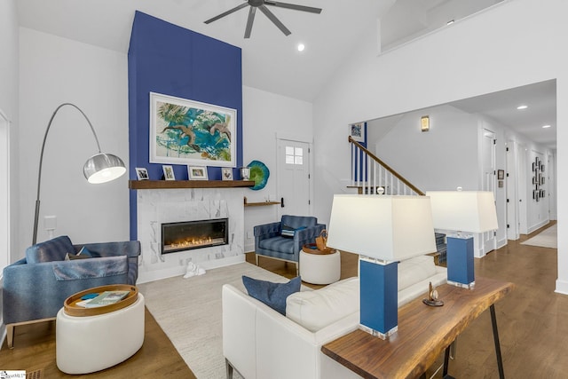 living area with recessed lighting, stairway, a glass covered fireplace, wood finished floors, and high vaulted ceiling