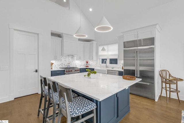 kitchen featuring wood finished floors, high end appliances, a breakfast bar area, and white cabinets