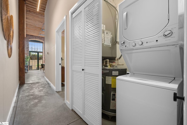 clothes washing area featuring laundry area, water heater, baseboards, and stacked washer and clothes dryer