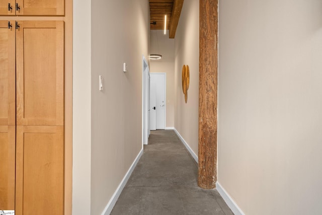 corridor with baseboards, concrete flooring, and beamed ceiling