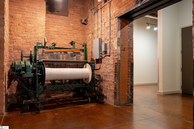 interior space featuring finished concrete flooring, brick wall, a towering ceiling, and baseboards