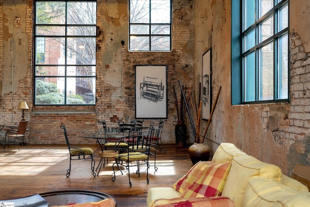 dining room with brick wall, wood-type flooring, and a towering ceiling