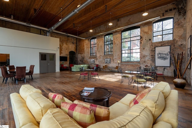 living room with brick wall, wood finished floors, and a towering ceiling