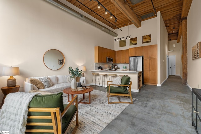 living area with baseboards, a towering ceiling, wooden ceiling, rail lighting, and finished concrete floors