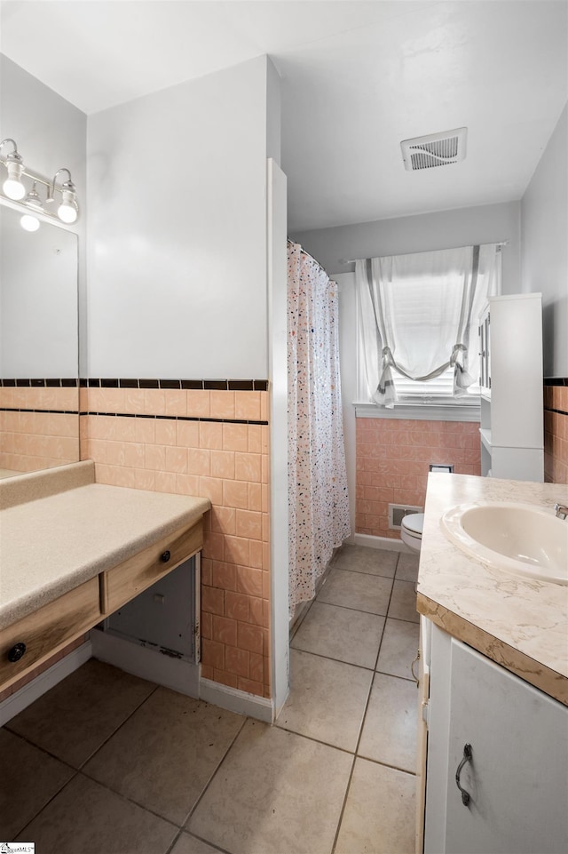 bathroom with a wainscoted wall, tile walls, vanity, visible vents, and tile patterned floors