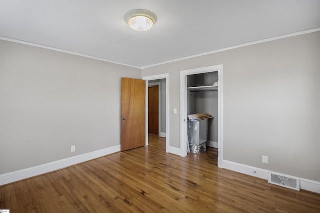 unfurnished bedroom with wood finished floors, visible vents, baseboards, a closet, and crown molding