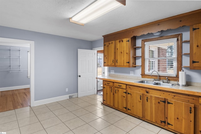 kitchen with light tile patterned floors, open shelves, brown cabinetry, and a sink