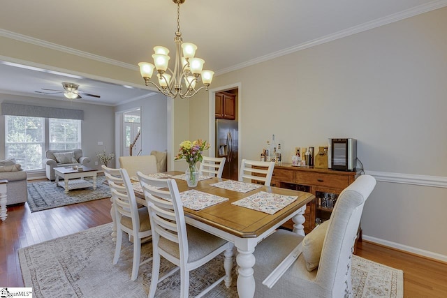 dining space featuring ceiling fan with notable chandelier, crown molding, baseboards, and wood finished floors