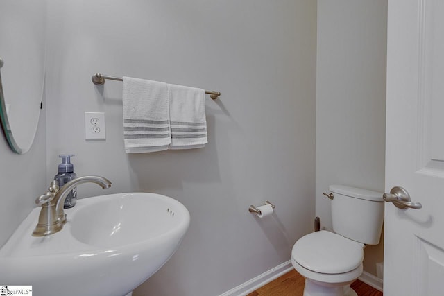 half bathroom with wood finished floors, a sink, toilet, and baseboards