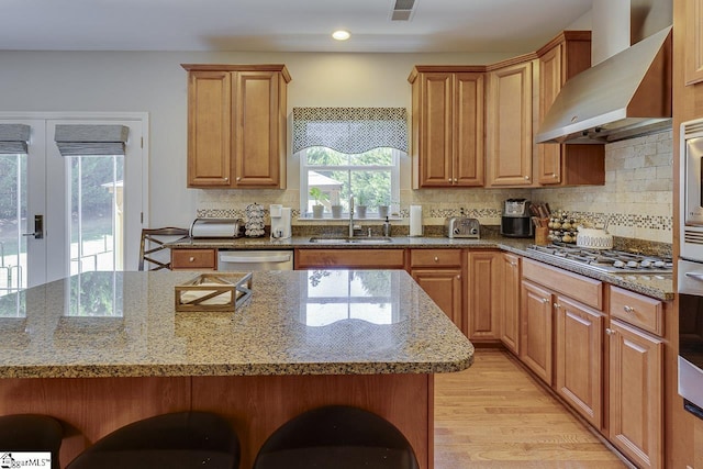 kitchen with a kitchen bar, light wood-style flooring, appliances with stainless steel finishes, a sink, and wall chimney exhaust hood