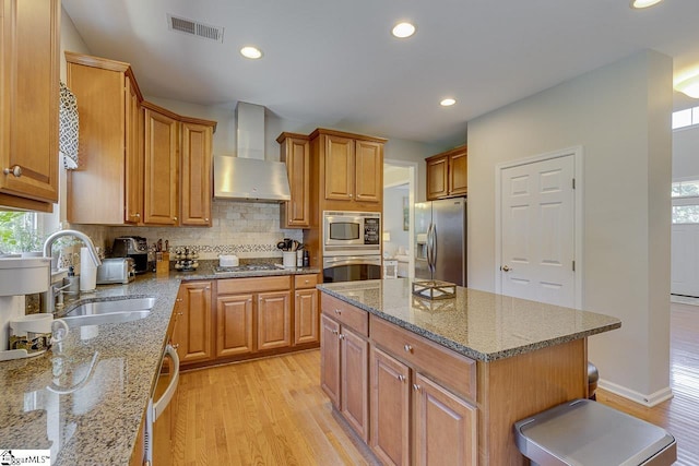 kitchen with visible vents, appliances with stainless steel finishes, light wood-style floors, a sink, and wall chimney exhaust hood