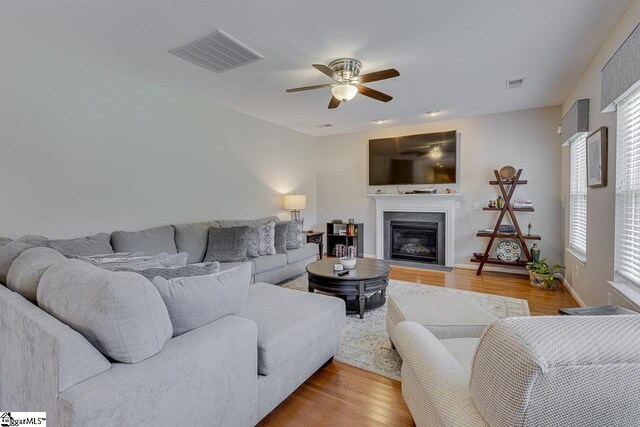 living area featuring ceiling fan, visible vents, wood finished floors, and a glass covered fireplace