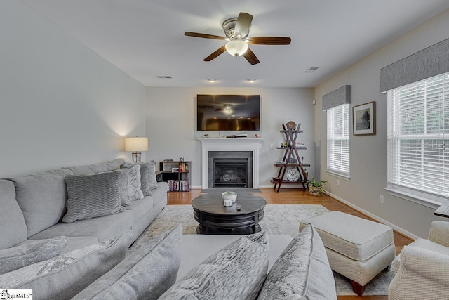 living area featuring a glass covered fireplace, wood finished floors, visible vents, and baseboards