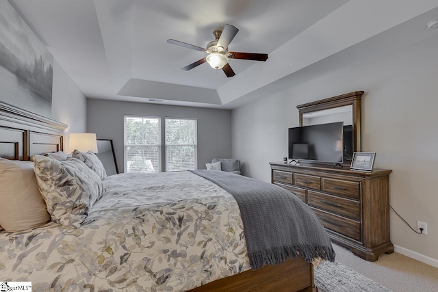 carpeted bedroom featuring a raised ceiling, ceiling fan, and baseboards