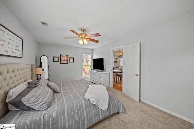 bedroom featuring baseboards, visible vents, light colored carpet, a textured ceiling, and ceiling fan with notable chandelier