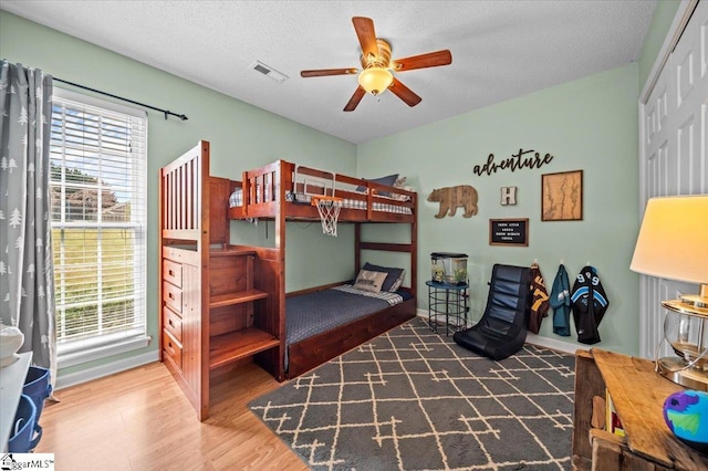 bedroom featuring a ceiling fan, visible vents, a textured ceiling, and wood finished floors