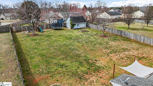 view of yard featuring a trampoline, a residential view, a fenced backyard, and an outdoor structure