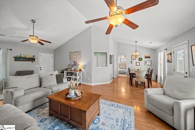 living room featuring ceiling fan with notable chandelier, visible vents, baseboards, vaulted ceiling, and light wood-type flooring