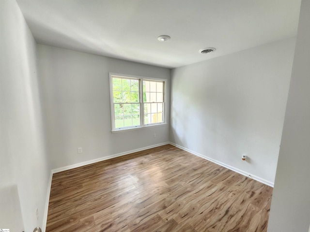 empty room featuring wood finished floors, visible vents, and baseboards