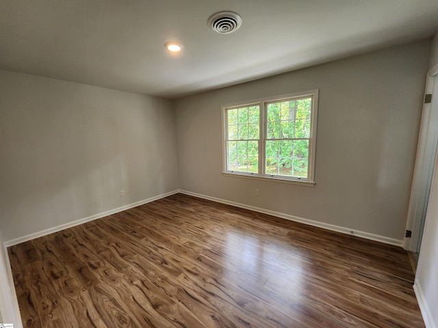 spare room featuring dark wood-type flooring, visible vents, and baseboards