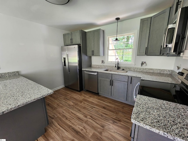 kitchen with light stone counters, dark wood-style floors, stainless steel appliances, hanging light fixtures, and a sink