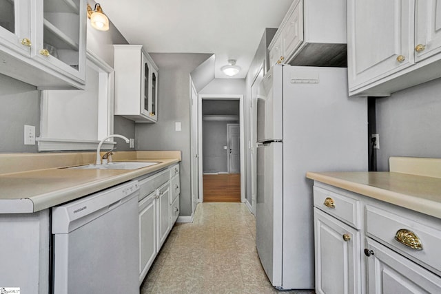 kitchen featuring white appliances, baseboards, glass insert cabinets, light countertops, and a sink