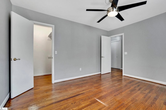 unfurnished bedroom featuring baseboards, a walk in closet, and wood finished floors