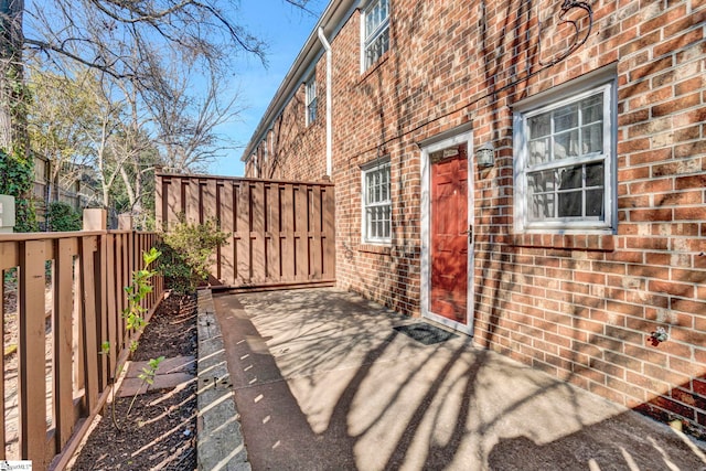 view of exterior entry with brick siding and fence