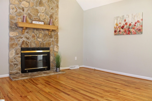 unfurnished living room featuring a fireplace, lofted ceiling, visible vents, wood finished floors, and baseboards