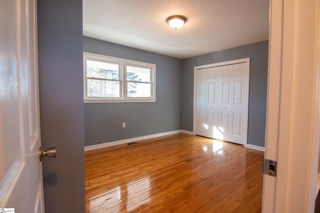 unfurnished bedroom featuring a closet, visible vents, baseboards, and hardwood / wood-style flooring