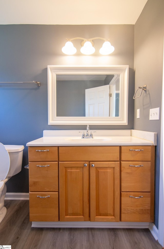 half bathroom with toilet, wood finished floors, vanity, and baseboards