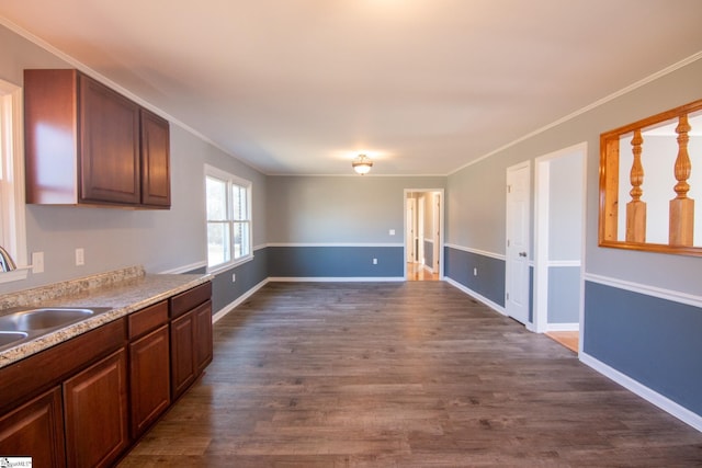 kitchen with baseboards, dark wood-style floors, ornamental molding, light countertops, and a sink